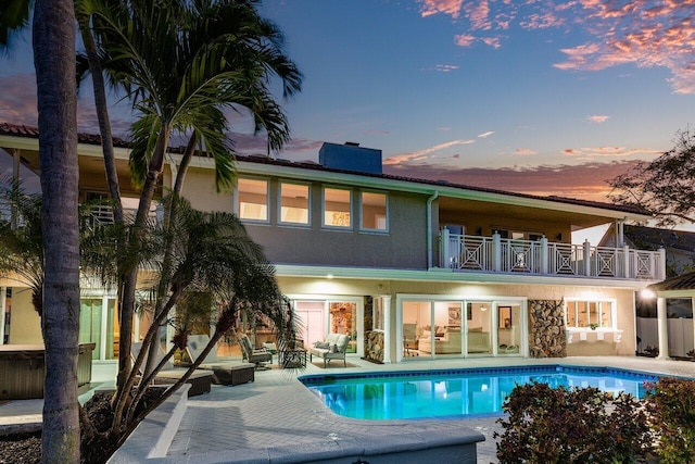 back house at dusk featuring a balcony and a patio