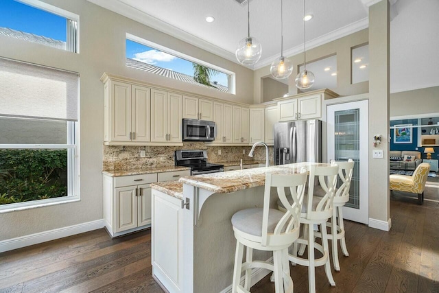 kitchen featuring a center island with sink, appliances with stainless steel finishes, decorative backsplash, light stone countertops, and pendant lighting