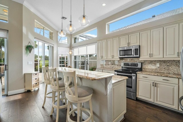 kitchen with stainless steel appliances, an island with sink, backsplash, hanging light fixtures, and light stone counters