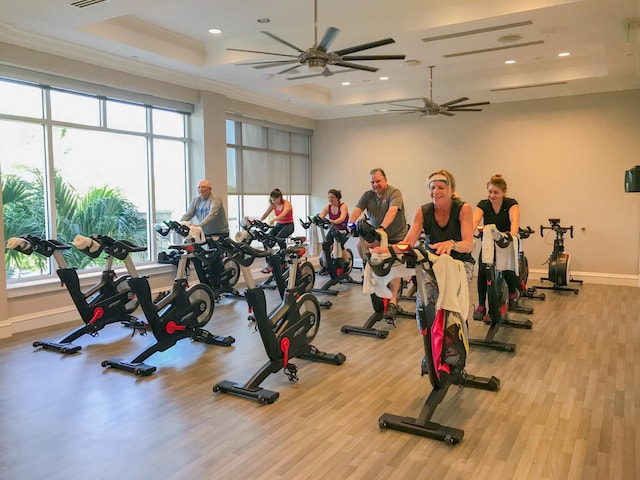 exercise room featuring ceiling fan, light hardwood / wood-style flooring, a raised ceiling, and ornamental molding