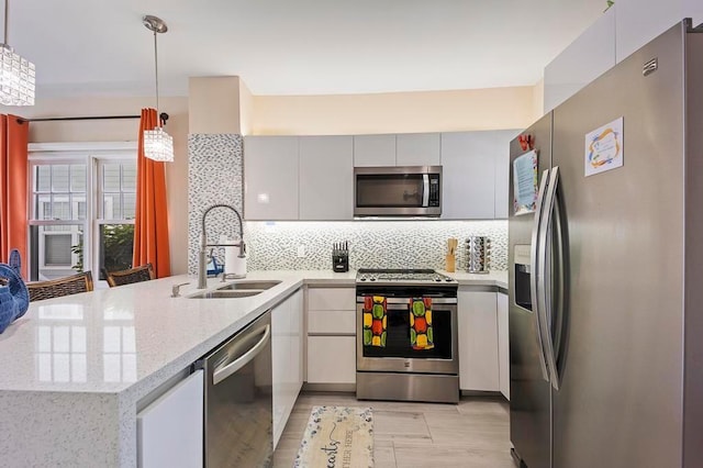 kitchen featuring kitchen peninsula, appliances with stainless steel finishes, backsplash, pendant lighting, and sink