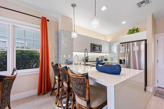 kitchen with kitchen peninsula, a breakfast bar area, appliances with stainless steel finishes, backsplash, and pendant lighting