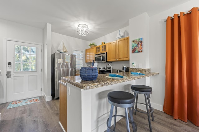 kitchen with kitchen peninsula, stainless steel appliances, a kitchen breakfast bar, dark stone counters, and light hardwood / wood-style flooring