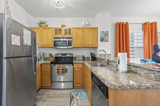 kitchen featuring stone counters, kitchen peninsula, sink, light hardwood / wood-style flooring, and appliances with stainless steel finishes