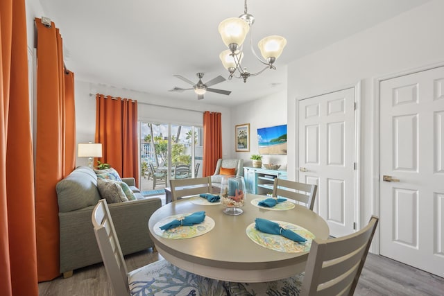 dining room featuring ceiling fan with notable chandelier and light hardwood / wood-style flooring