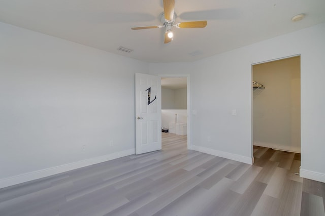 unfurnished bedroom featuring a closet, a walk in closet, light hardwood / wood-style floors, and ceiling fan