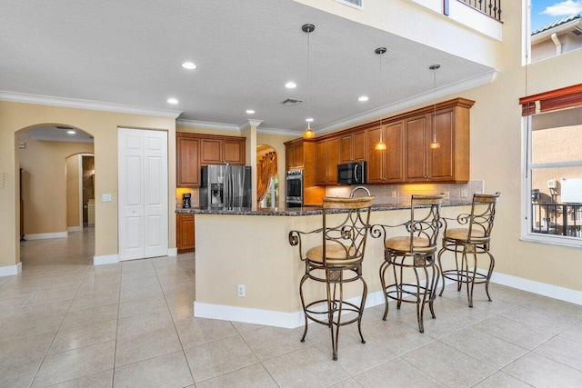 kitchen with hanging light fixtures, stainless steel appliances, dark stone countertops, ornamental molding, and light tile patterned flooring