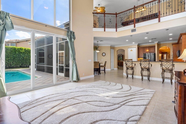 living room featuring ceiling fan, a high ceiling, crown molding, and light tile patterned floors