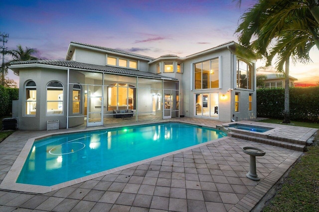 back house at dusk featuring a pool with hot tub, a sunroom, and a patio