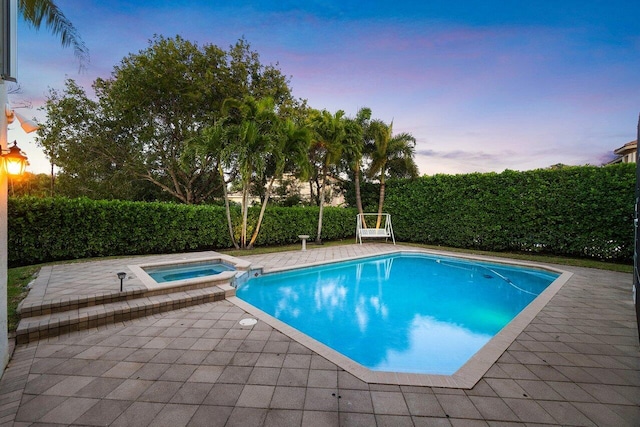 pool at dusk featuring a patio area and an in ground hot tub