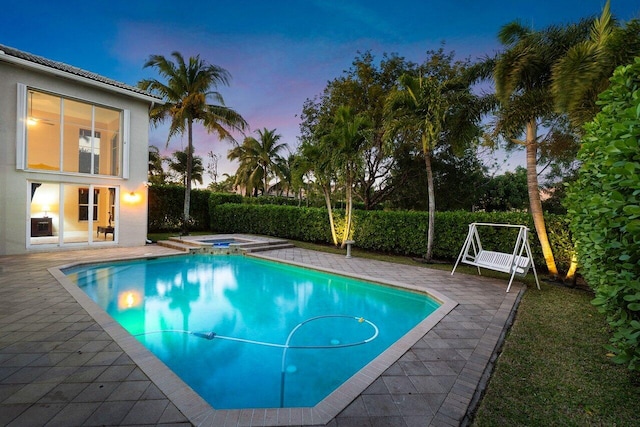 pool at dusk featuring a patio area and an in ground hot tub