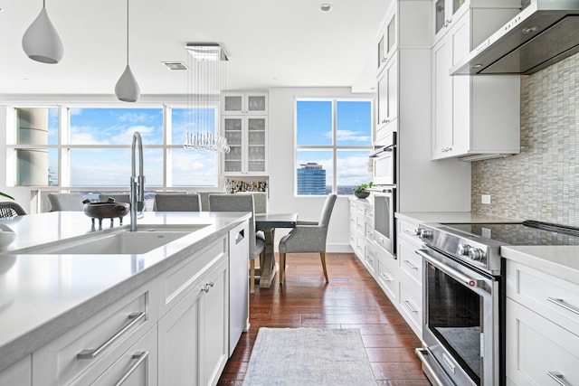 kitchen featuring white cabinets, appliances with stainless steel finishes, wall chimney exhaust hood, decorative light fixtures, and backsplash