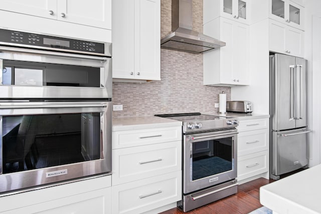 kitchen featuring wall chimney exhaust hood, white cabinetry, stainless steel appliances, decorative backsplash, and dark hardwood / wood-style floors