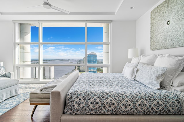 bedroom with floor to ceiling windows, wood-type flooring, a water view, and ceiling fan