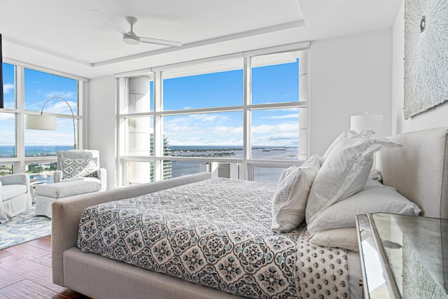 bedroom with ceiling fan, multiple windows, a water view, and floor to ceiling windows