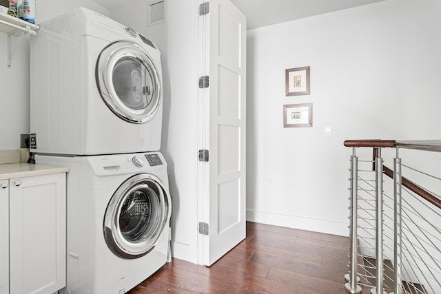 laundry area with cabinets, stacked washer and clothes dryer, and dark hardwood / wood-style flooring