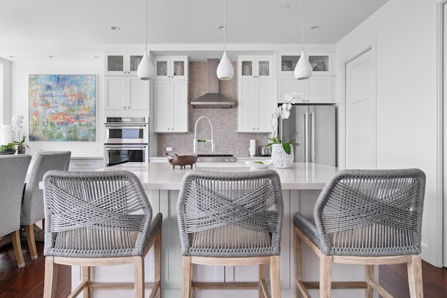 kitchen with pendant lighting, white cabinetry, wall chimney exhaust hood, and stainless steel appliances