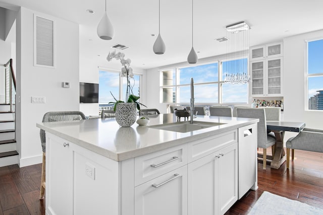 kitchen with decorative light fixtures, a center island with sink, sink, white cabinetry, and dark hardwood / wood-style flooring