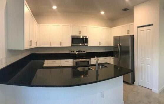 kitchen featuring appliances with stainless steel finishes, white cabinetry, kitchen peninsula, and sink