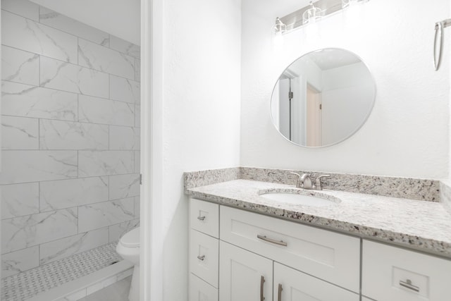 bathroom featuring a tile shower, vanity, and toilet