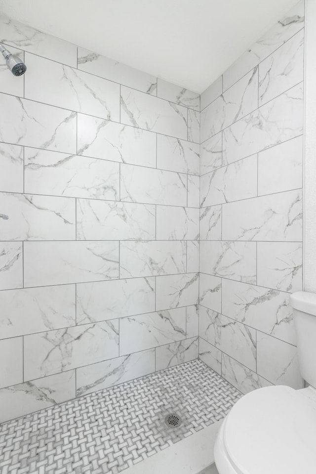 bathroom with a tile shower and toilet