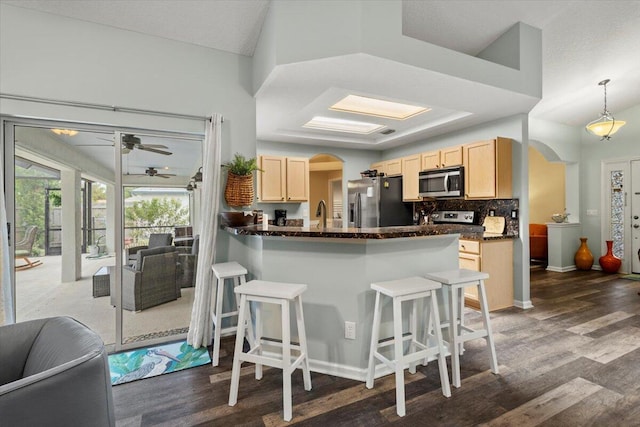 kitchen with appliances with stainless steel finishes, pendant lighting, a kitchen bar, light brown cabinetry, and decorative backsplash