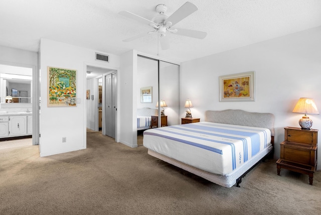 carpeted bedroom with a textured ceiling, ceiling fan, a closet, and ensuite bath