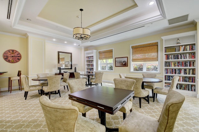 living room featuring a raised ceiling, a notable chandelier, built in shelves, and crown molding