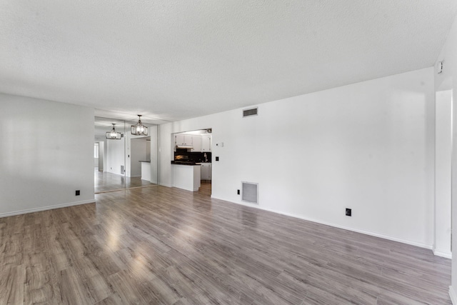 unfurnished living room featuring a textured ceiling, hardwood / wood-style floors, and a notable chandelier