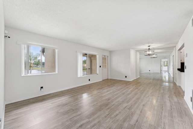 unfurnished living room featuring a textured ceiling, a notable chandelier, light hardwood / wood-style floors, and plenty of natural light