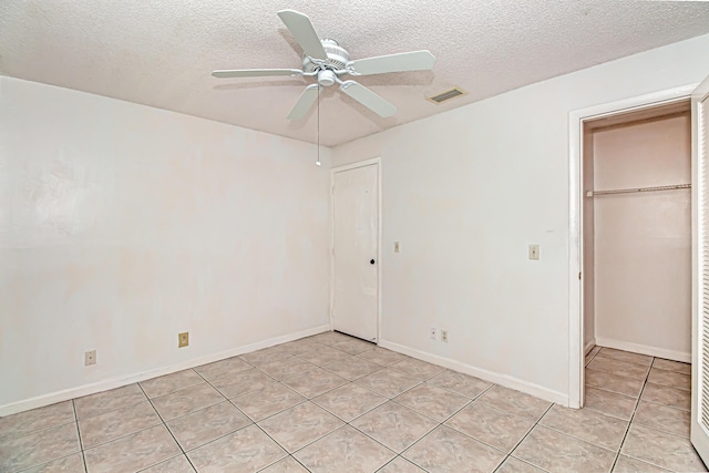 unfurnished bedroom with ceiling fan, a textured ceiling, light tile patterned floors, and a closet