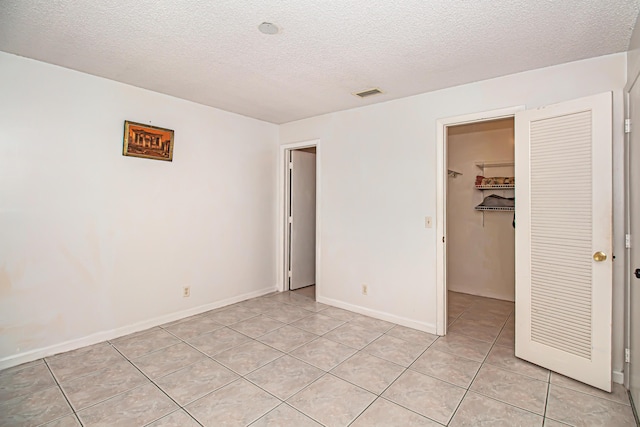 unfurnished bedroom with a walk in closet, a closet, light tile patterned flooring, and a textured ceiling