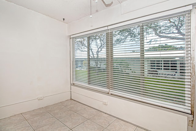 empty room with ceiling fan, a textured ceiling, light tile patterned floors, and a wealth of natural light