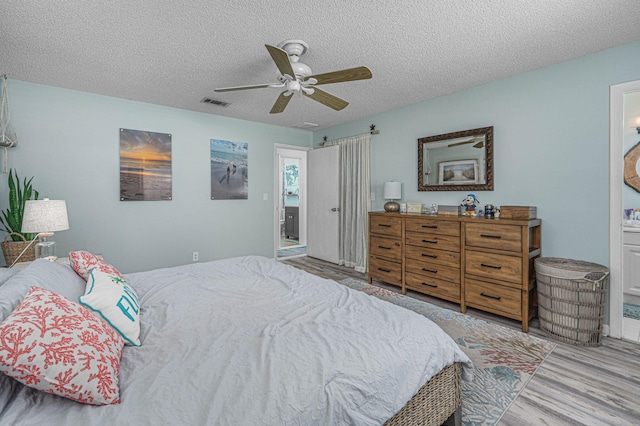 bedroom featuring ceiling fan, light hardwood / wood-style floors, ensuite bathroom, and a textured ceiling