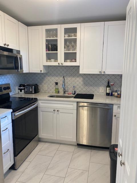 kitchen with sink, white cabinets, light tile patterned floors, decorative backsplash, and appliances with stainless steel finishes