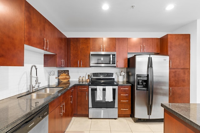 kitchen featuring sink, light tile patterned flooring, dark stone counters, and appliances with stainless steel finishes