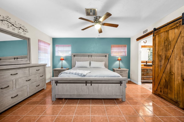 bedroom with a barn door, tile patterned floors, ceiling fan, and ensuite bath