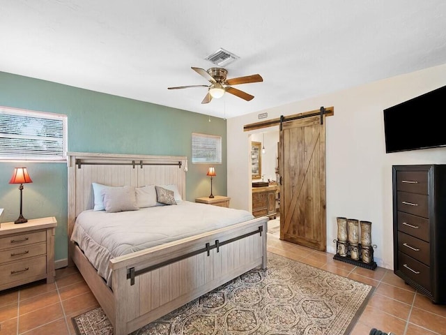 bedroom featuring ceiling fan, ensuite bathroom, a barn door, and tile patterned floors