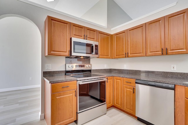 kitchen with appliances with stainless steel finishes, vaulted ceiling, and light hardwood / wood-style floors