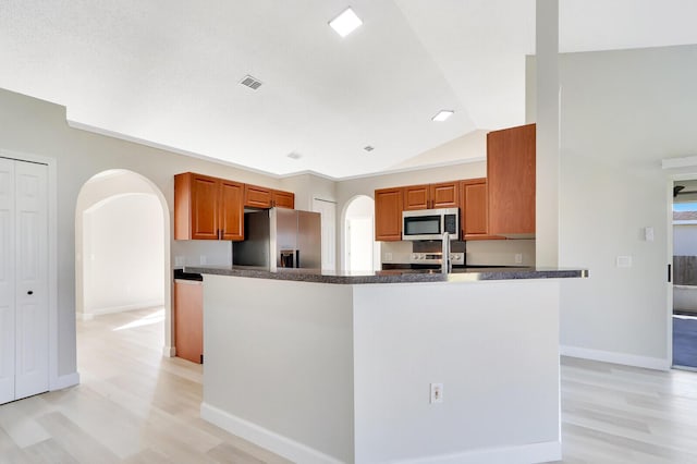 kitchen featuring kitchen peninsula, stainless steel appliances, light hardwood / wood-style floors, and lofted ceiling