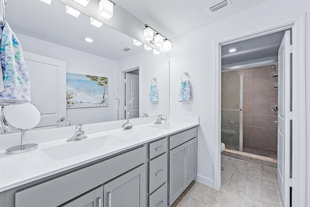 bathroom featuring a textured ceiling, a shower with door, vanity, and toilet