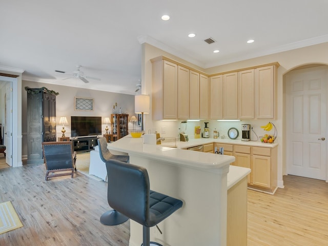 kitchen featuring ornamental molding, light hardwood / wood-style floors, a breakfast bar area, and kitchen peninsula