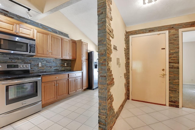 kitchen featuring light tile patterned flooring, appliances with stainless steel finishes, vaulted ceiling, and backsplash