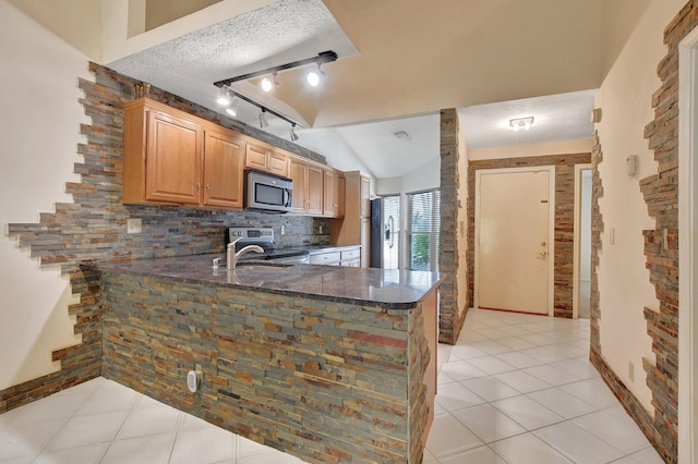 kitchen featuring a textured ceiling, vaulted ceiling, light tile patterned floors, kitchen peninsula, and appliances with stainless steel finishes