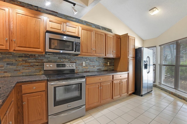 kitchen featuring appliances with stainless steel finishes, vaulted ceiling, decorative backsplash, and light tile patterned floors