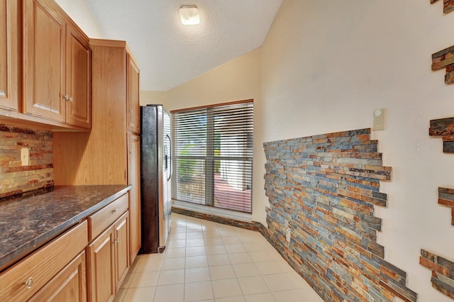 kitchen featuring dark stone countertops, light tile patterned floors, stainless steel fridge, a textured ceiling, and lofted ceiling