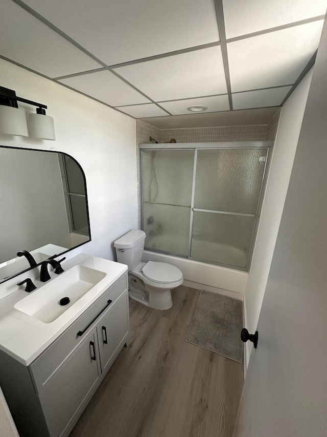 full bathroom featuring combined bath / shower with glass door, hardwood / wood-style flooring, a paneled ceiling, toilet, and vanity