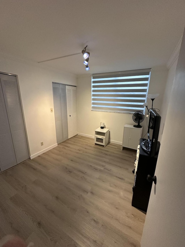 unfurnished bedroom featuring hardwood / wood-style flooring, ceiling fan, crown molding, and two closets