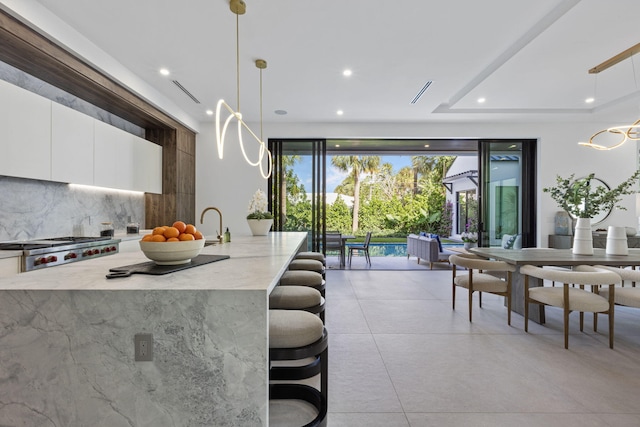 kitchen featuring light stone countertops, pendant lighting, white cabinets, and range