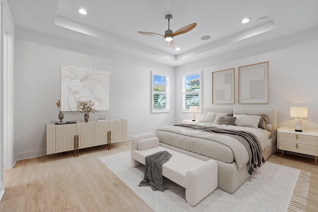 bedroom with ceiling fan, radiator heating unit, light hardwood / wood-style floors, and a tray ceiling